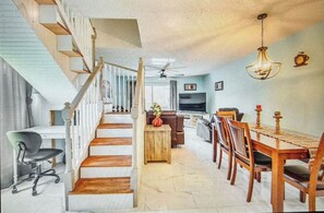 A spacious living area with a staircase, a dining table with chairs, a sofa, and a television. - Lakeside Serenity Retreat  (Inverness)