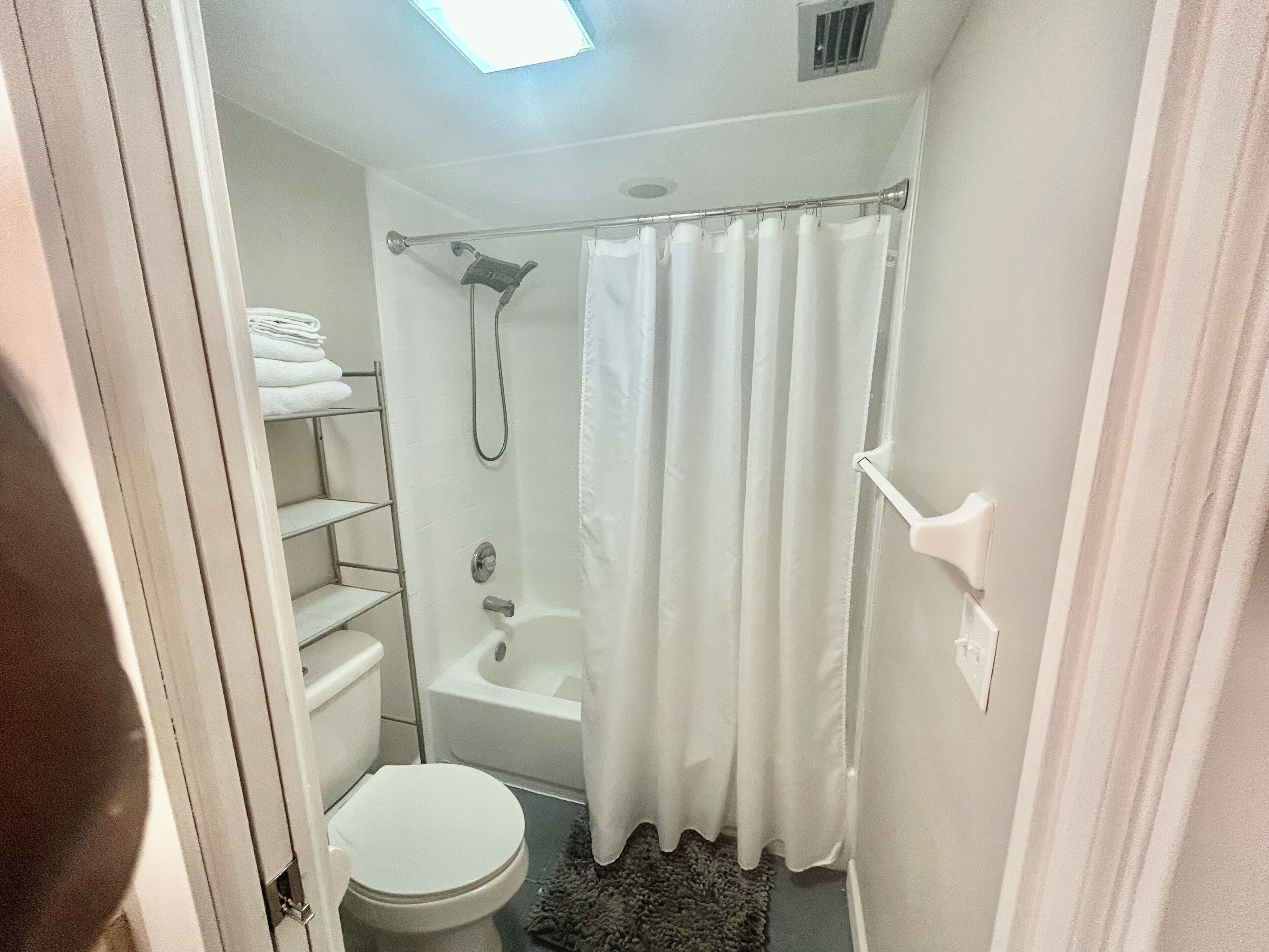 Et lille, kompakt badeværelse med toilet, bruser med gardin og en hylde med håndklæder.