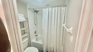 Et lille, kompakt badeværelse med toilet, bruser med gardin og en hylde med håndklæder.