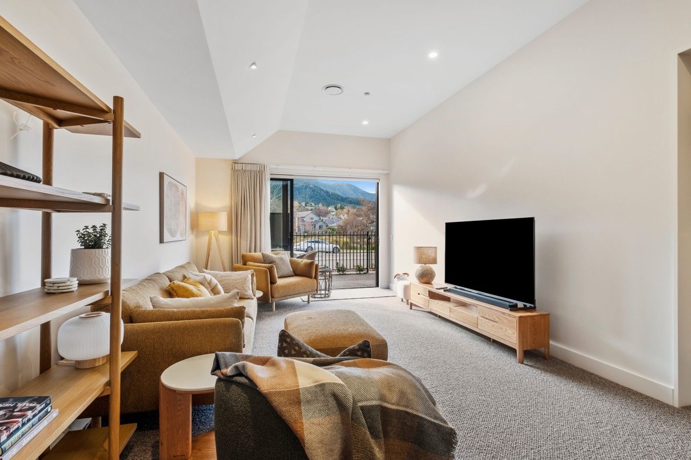 A modern living room with a sofa, armchairs, a TV, and a balcony with a view.