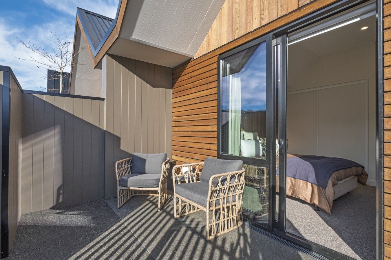 A modern outdoor seating area with wicker furniture and a glass door leading to a bedroom.