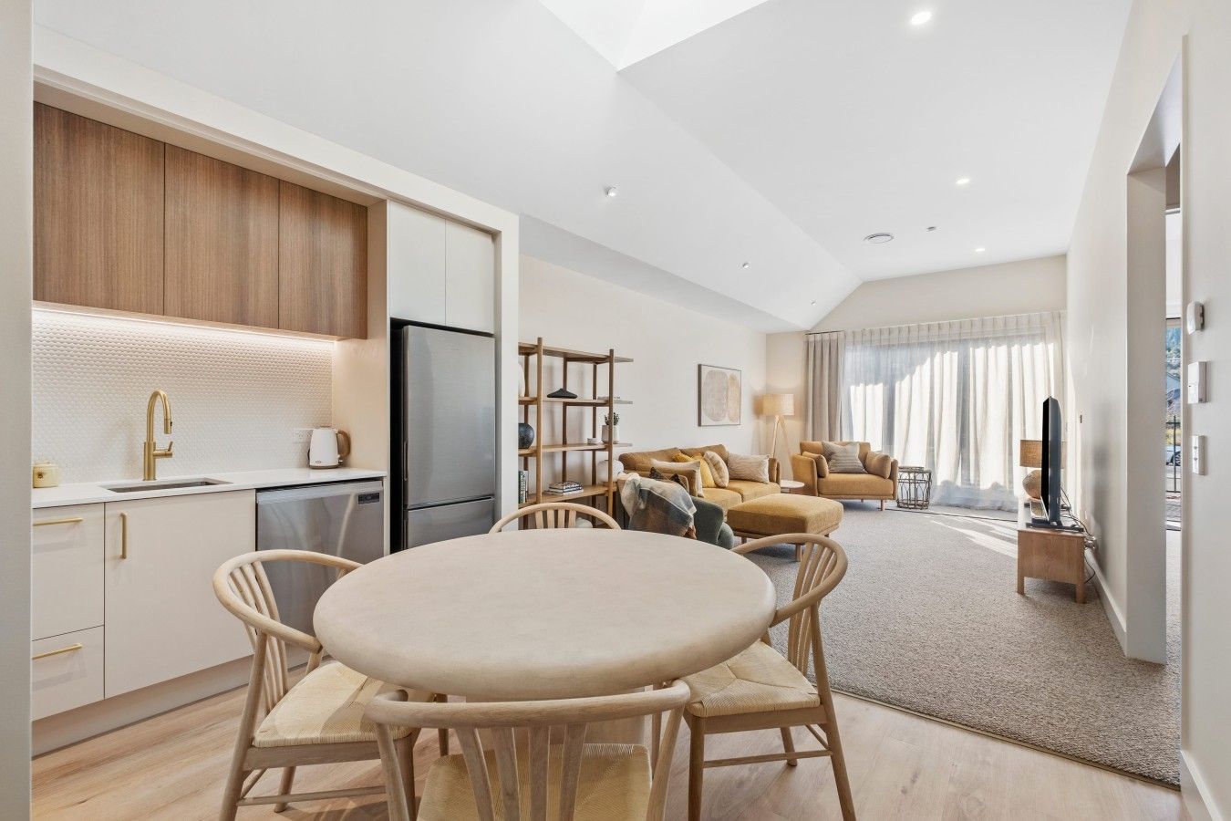 A modern kitchen with a dining area, a living room with sofas, and a TV.