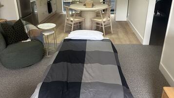 Een modern appartement met een centraal gelegen eethoek, een bank en een bed met een gestreept dekbed.