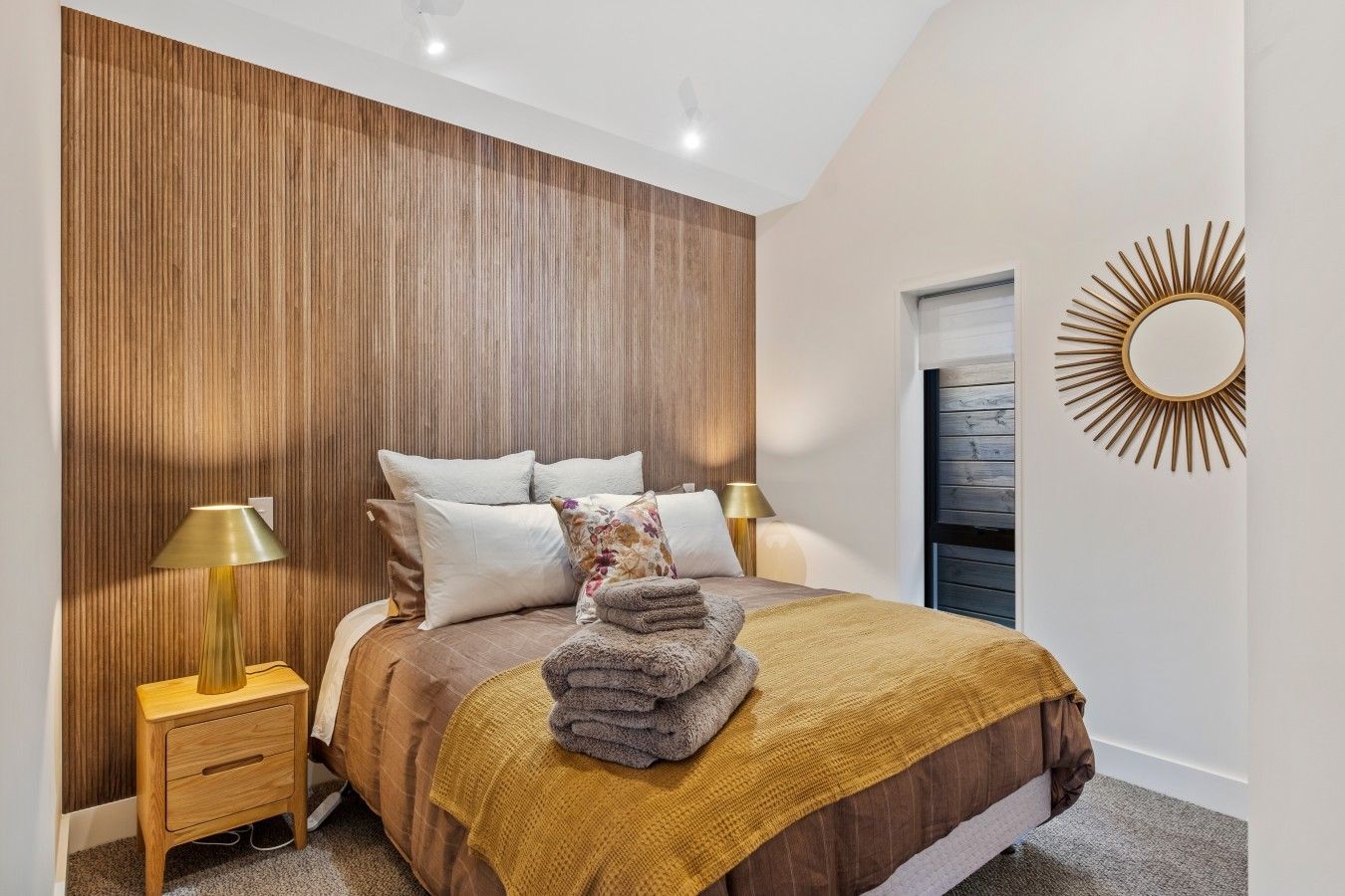 A bedroom with a bed, bedside lamps, a mirror, and a wooden panel wall.