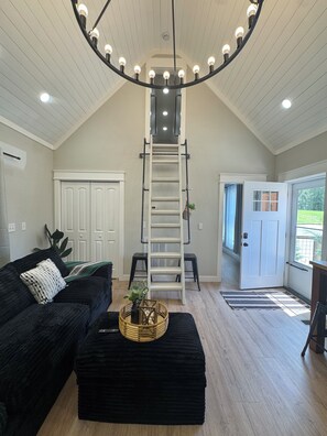 A room with a black sofa, a white door, a wooden floor, and a ceiling with a circular light fixture.