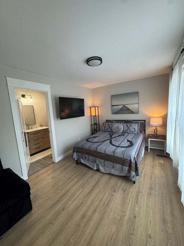 A bedroom with a bed, a TV, a bedside table, a lamp, and a painting on the wall.