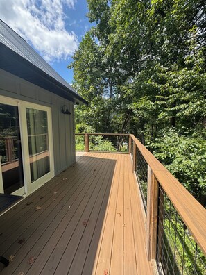 A wooden deck with a glass door leading to a covered area, surrounded by trees.