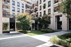 Un edificio residencial de varios pisos con balcones, un patio con vegetación y un diseño arquitectónico moderno.