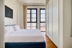 A hotel room with a large bed, a view of the city through the windows, and a door leading to an outdoor balcony. - w* | Luxury 1BR in Milan (Milano)