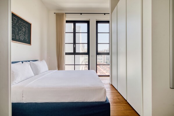 Una camera d'hotel con un letto grande, vista sulla città dalle finestre e una porta che dà su un balcone all'aperto.