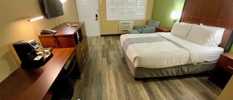 A hotel room with a bed, desk, chair, TV, and a window with blinds.