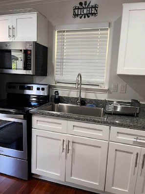 A kitchen with white cabinets, a stainless steel sink, a microwave, and a stove. - La Casita private & quiet with great location area (San Antonio)