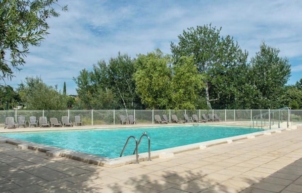 A swimming pool with a tiled deck, surrounded by a fence and trees.