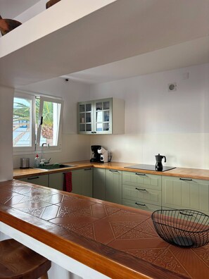 A kitchen with a wooden countertop, a sink, a cabinet, and a window with a view of palm trees. - Villa Lava - 3-Bedroom Villa in Downtown Puerto del Carmen (Tías)