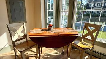 A dining area with a wooden table and chairs, large windows, and a view of the outside.