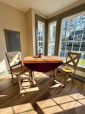 A dining area with a wooden table and chairs, large windows, and a view of the outside.