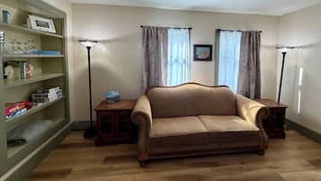 A living room with a brown sofa, a wooden side table, a bookshelf, and two floor lamps.