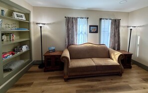 Una sala de estar con un sofá marrón, una mesita de madera, una estantería y dos lámparas de pie.