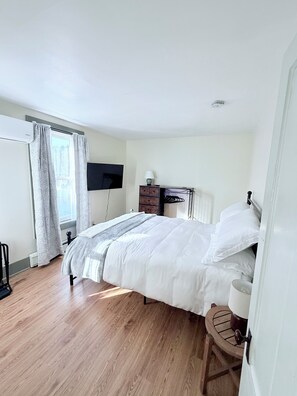 A bedroom with a bed, a TV mounted on the wall, a dresser, and a window with curtains.