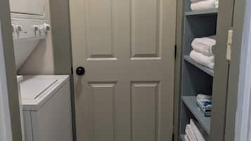 A laundry room with a door, a washing machine, and shelves with folded towels.