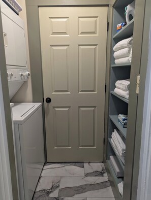 A laundry room with a door, a washing machine, and shelves with folded towels.