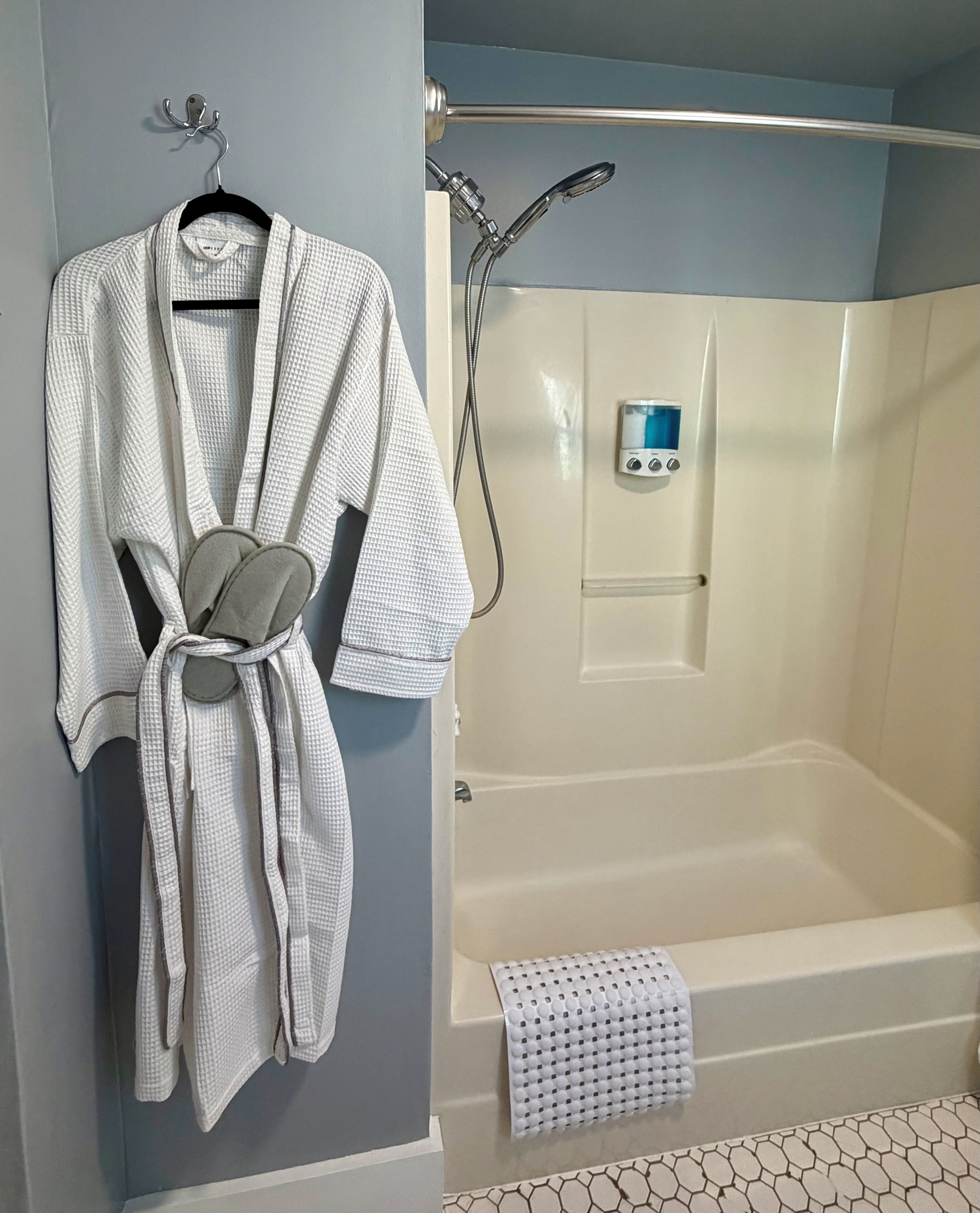 A bathroom with a bathtub, a towel rack with a robe, and a shower control panel.