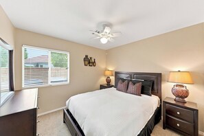 Quarto com cama, mesas de cabeceira, ventoinha no teto e janela com persianas.
