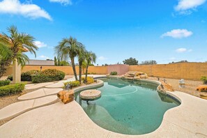 Piscina com design curvo, rodeada por um deck de concreto e palmeiras.