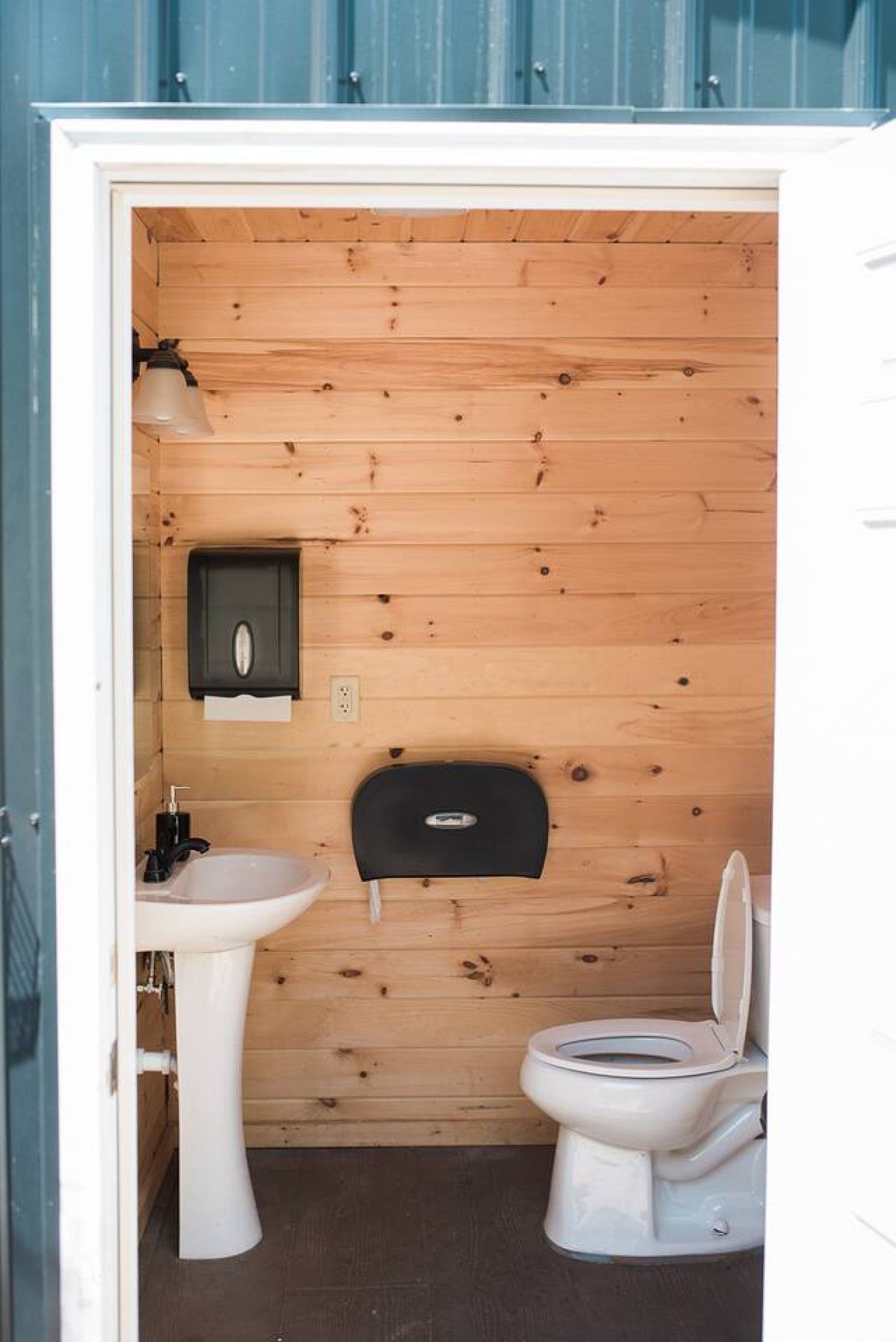 Un bagno compatto con una parete in legno, un lavandino bianco, un WC e un piccolo mobiletto nero.