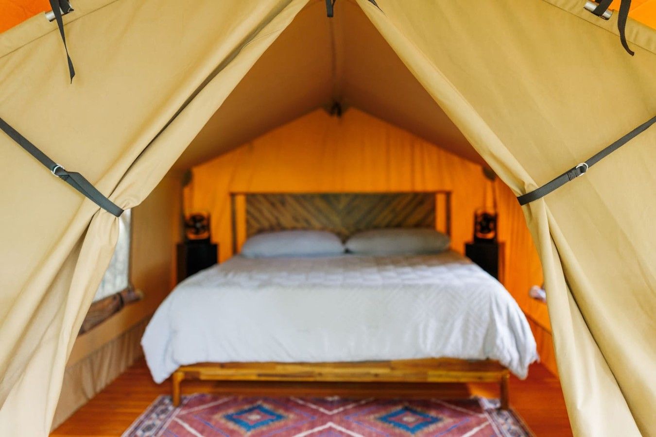 Une pièce aménagée comme une tente, avec un lit, une tête de lit en bois et un tapis à motifs.
