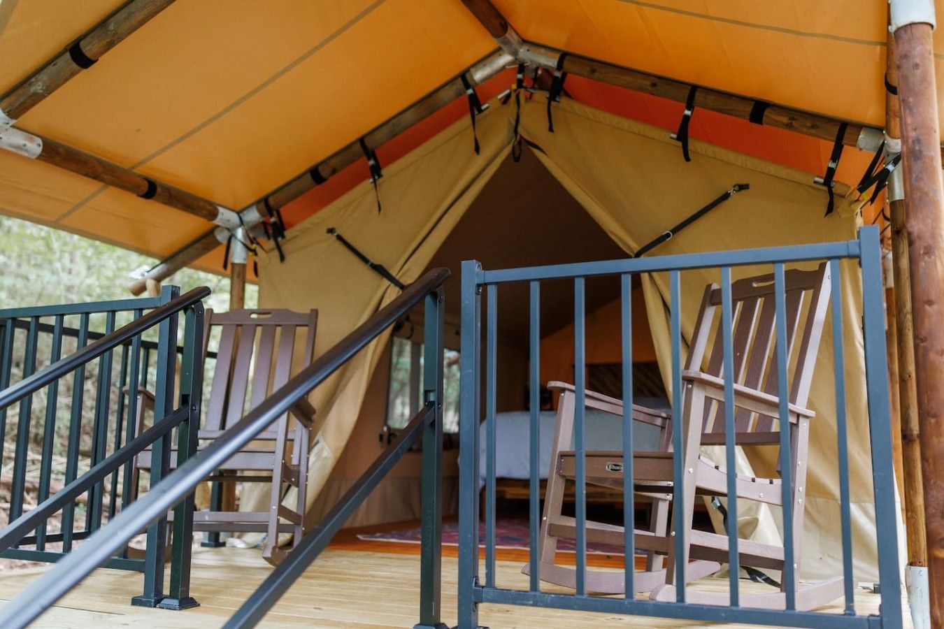 Une tente avec une rambarde en métal et des chaises en bois à l’intérieur.