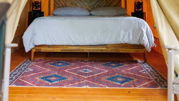 Uma tenda com cama, um tapete estampado e uma cabeceira de madeira.