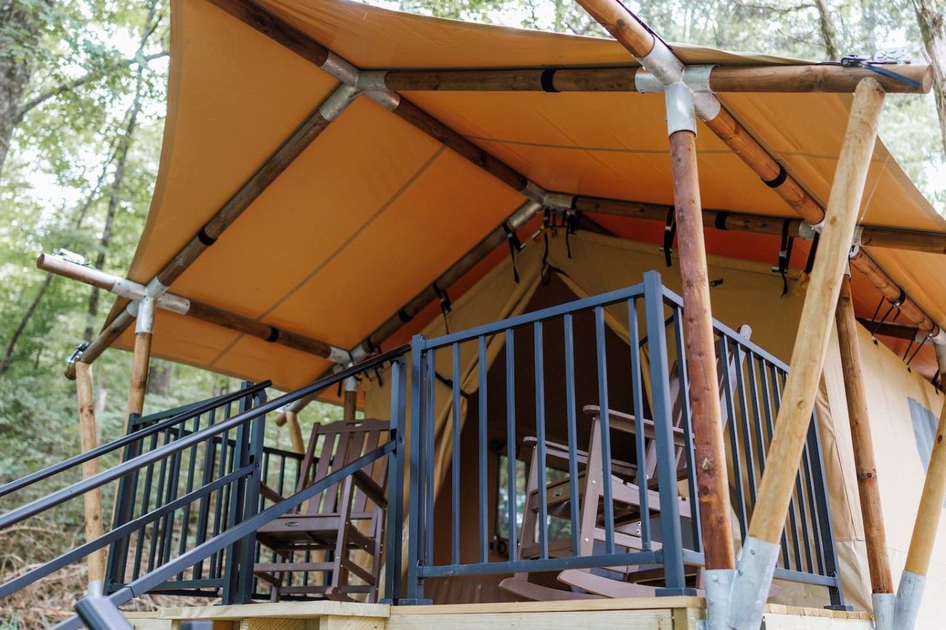 A tent with a wooden staircase and railings, surrounded by trees.