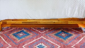 Uma cama de solteiro com cabeceira de madeira, roupa de cama branca e tapete estampado no chão.
