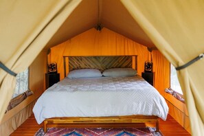 A tent with a bed, two bedside tables, and a patterned rug.