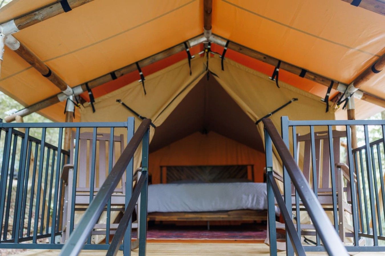 A tented accommodation with a bed, railings, and a view of the outdoors.