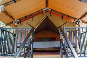 A tented accommodation with a bed, railings, and a view of the outdoors.