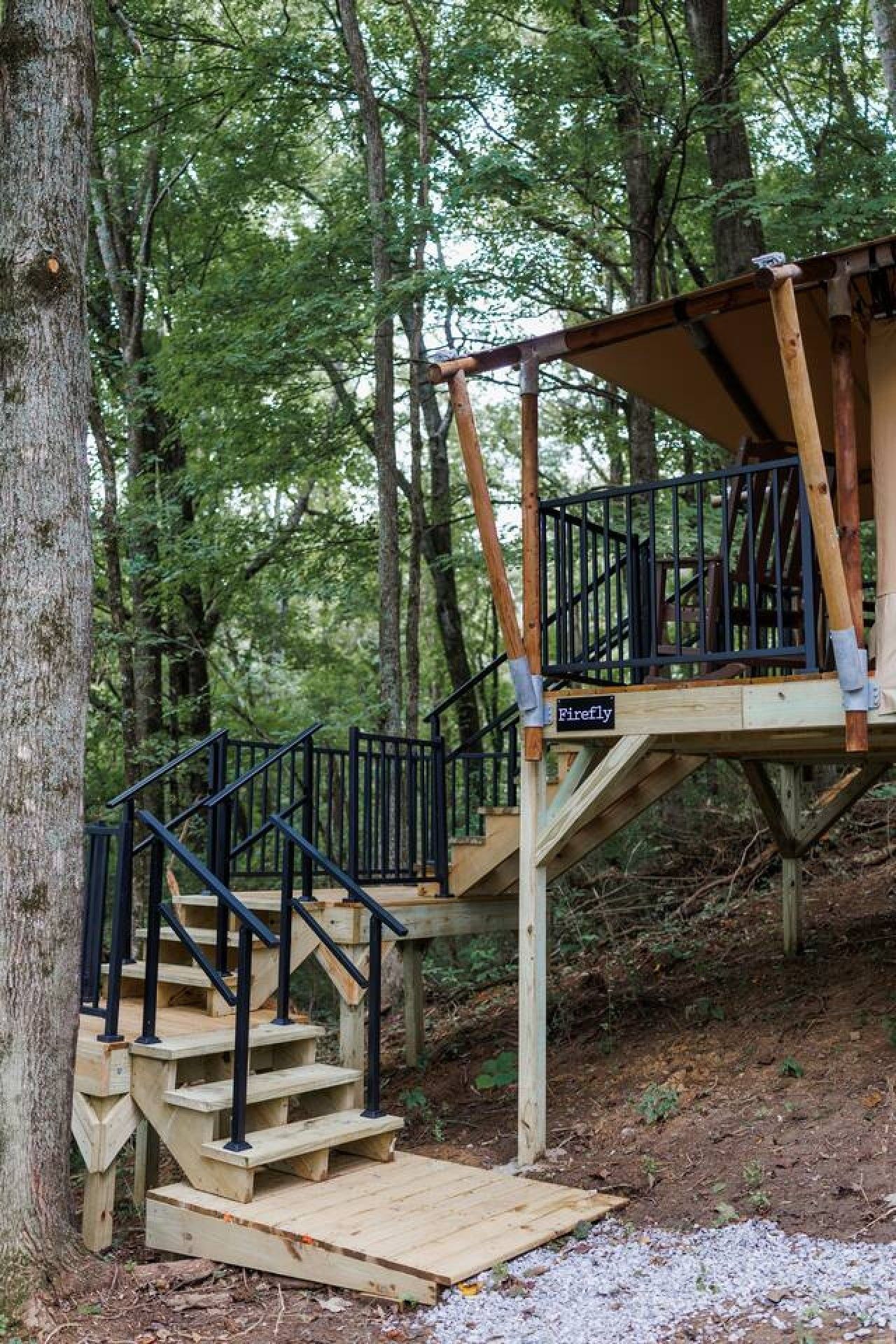 Een houten trap die leidt naar een terras met een 'Firefly' bord, omringd door bomen.