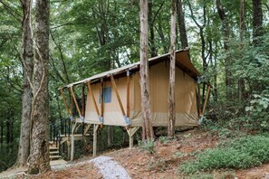 A treehouse with a simple wooden structure and a tarp roof, surrounded by dense forest.