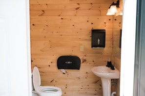 Ett badrum med träpanel på väggarna, utrustat med toalett, handfat och en svart tvåldispenser.