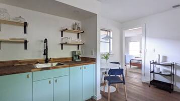 A kitchen with light blue cabinets, a wooden countertop, and a coffee machine. There is a dining area with a white table and blue chairs.
