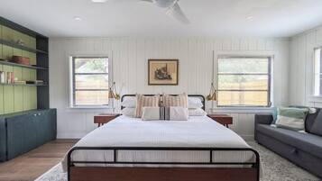 A bedroom with a bed, a ceiling fan, a window with blinds, a bookshelf, and a gray sofa.