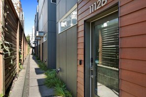 A narrow alleyway with a wooden fence on one side and a modern building with a large glass door on the other. - Artist's Townhouse in Capitol Hill w/ AC + Rooftop (Seattle)