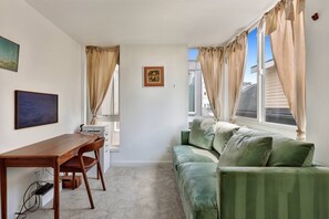 A room with a green sofa, a wooden desk, and a window with curtains. - Artist's Townhouse in Capitol Hill w/ AC + Rooftop (Seattle)