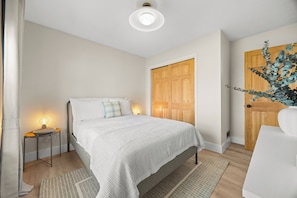 A bedroom with a bed, bedside table, lamp, and a wooden door.