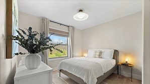 A bedroom with a bed, bedside tables, a nightstand, a window with curtains, a ceiling light, and a potted plant. - Perched Above Cayuga ·  Sauna · Winery On-Site (Romulus)