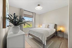 A bedroom with a bed, bedside tables, a nightstand, a window with curtains, a ceiling light, and a potted plant. - Perched Above Cayuga ·  Sauna · Winery On-Site (Romulus)