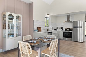 Een moderne keuken met witte kasten, roestvrijstalen apparatuur en een eethoek met rieten stoelen.