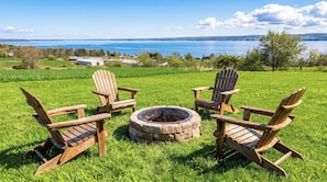 A grassy outdoor area with four wooden Adirondack chairs and a stone fire pit.