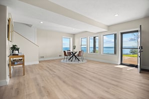 A spacious room with a dining area, large windows, and a view of the sea.